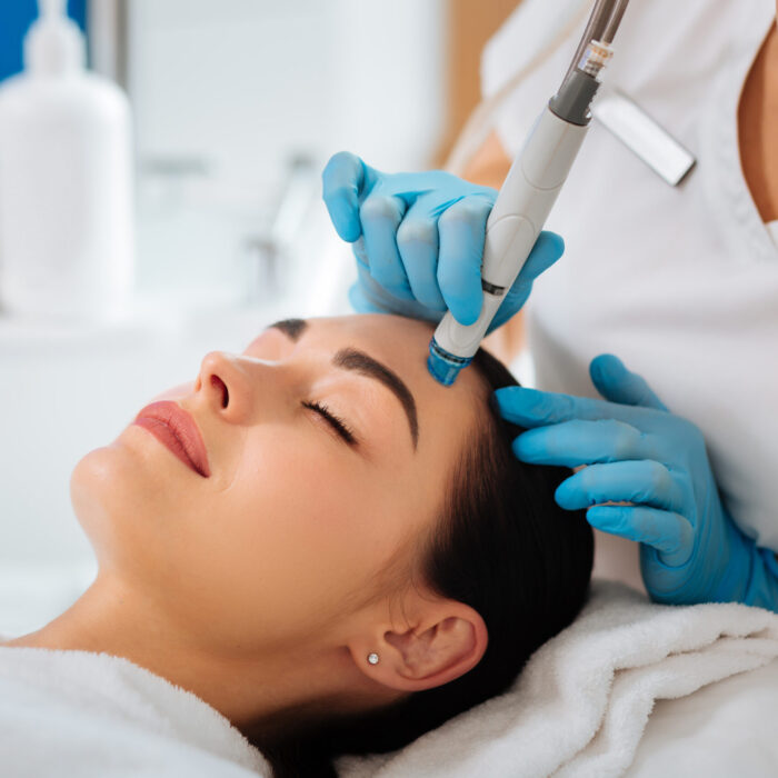 Professional cosmetology. Smart skilled cosmetologist using a modern device while doing hydrafacial procedure